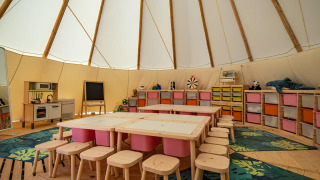 Indendørs børneområde i et tipitelt med farverige stole, borde, legetøj og opbevaringskasser i Grand Kažela.