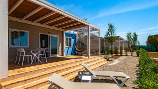Outdoor terrace of Camping Home Next chalet with sun loungers and dining set under a clear blue sky.