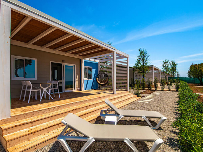 Terrazza esterna dello chalet Camping Home Next con lettini prendisole e tavolo sotto cielo sereno.