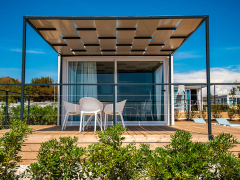 Ein modernes Chalet mit Terrasse und Gartenmöbeln im Camping Arena Grand Kažela in Kroatien bei Sonnenschein.