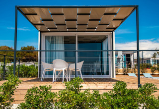 Ein modernes Chalet mit Terrasse und Gartenmöbeln im Camping Arena Grand Kažela in Kroatien bei Sonnenschein.