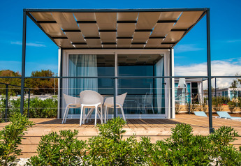 En moderne chalet med terrasse og havemøbler på Camping Arena Grand Kažela i Kroatien under blå himmel.