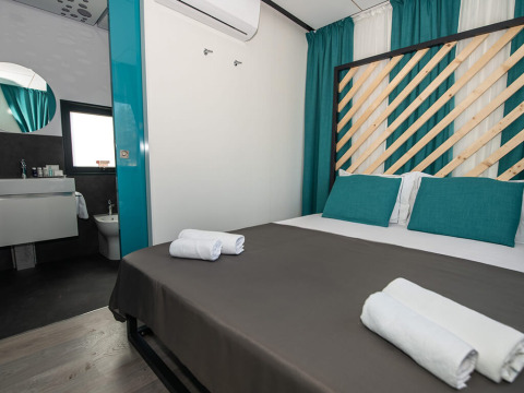 Modernes Chalet-Schlafzimmer mit Doppelbett, türkisfarbenen Kissen, und offenem Badbereich mit Handtüchern.