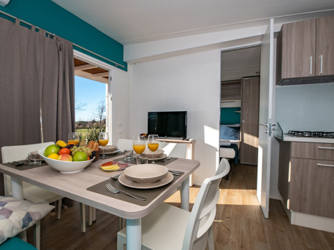 Essbereich für vier Personen in modernem Chalet mit Obstschale, Saft und Blick ins Schlafzimmer.