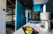 Cocina moderna de chalet con cafetera, bandeja de frutas frescas y literas en el fondo del ambiente.