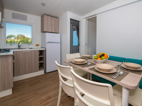 Modernes Chalet mit Küche, Esstisch für vier Personen, Obstschale und Blick auf die Natur draußen.