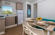 Modern chalet kitchen and dining area set for four, with fruit bowl and window view of green outdoors.