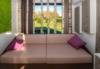 Moderne chaletinteriør med sofa, birkestammer foran vindue og grøn udsigt, Camping Home Green, Kroatien.