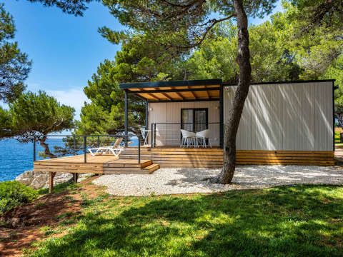 Deluxe Camping Villa First Row con vista mare, terrazza in legno e mobili moderni sotto i pini.