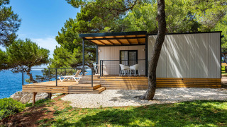 Deluxe Camping Villa First Row mit Meerblick, Holzterrasse und modernen Möbeln unter Kiefern.