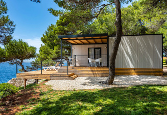 Deluxe Camping Villa First Row med havudsigt, træterrasse og moderne møbler under pinjetræer.