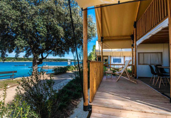 Two-bedroom glamping safari tent with wooden deck overlooking the water at Camping Arena Stoja, Croatia.