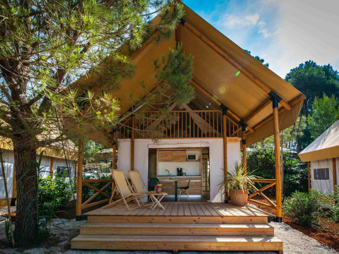 Two bedroom glamping safari loft tent with wooden deck, lounge chairs, and surrounded by greenery.
