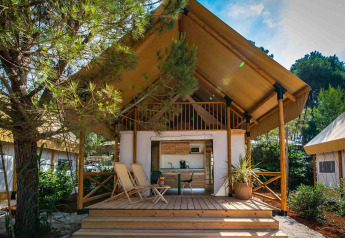 Tenda safari glamping loft con due camere da letto, veranda in legno, sedie e circondata dal verde.