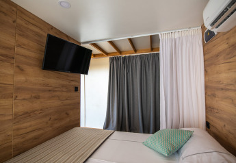 Interior of a glamping safari tent with wood walls, TV, air conditioning, and bed at Camping Arena Stoja, Croatia.