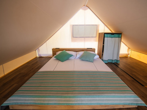 Vista interior de tienda safari loft con cama doble y armario en Camping Arena Stoja, Croacia.