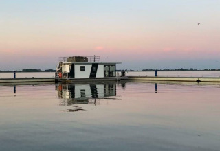 Zicht op een modern glampinghuisje op het water bij zonsondergang in een vakantiepark met spiegelende rust.