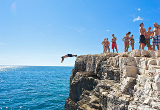 Group of people at Camping Arena Stoja in Istria, Croatia, watching someone cliff jump into the sparkling sea.