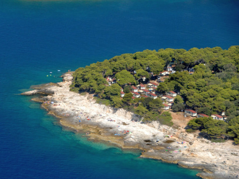 Vista aerea di Camping Arena Stoja in Istria, Croazia, con bungalow tra pini, costa rocciosa e mare blu.