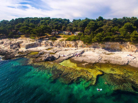 Vista aerea del Camping Arena Stoja a Pola, Istria, Croazia, con scogliera, pini e mare limpido.