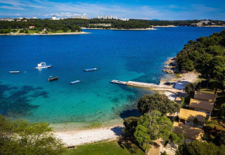 Luftfoto af Camping Arena Stoja i Istrien, Kroatien med klart blåt hav, både og strand omgivet af skov.