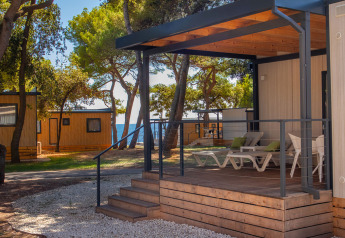 Deluxe Camping Villa Sea View, terrasse moderne avec transats, entourée d'arbres et vue partielle sur la mer.