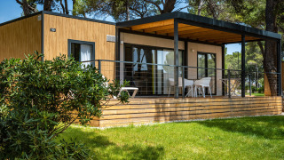 Modern lodge at Camping Villa featuring a wooden facade, spacious veranda, seating area, and greenery.
