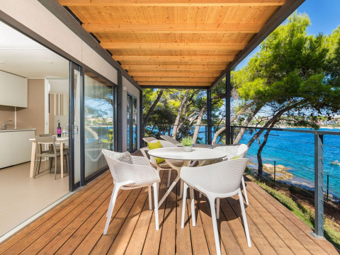 Covered wooden deck with dining set, sea views and trees at Camping Villa First Row, Arena Stoja, Croatia.
