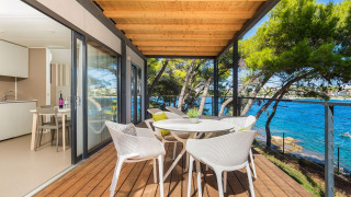 Overdekt houten terras met moderne stoelen en uitzicht op zee bij Camping Villa First Row, Arena Stoja.