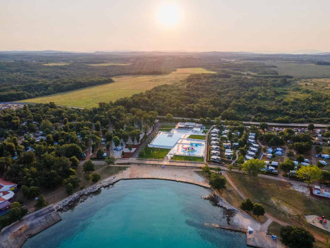Aerial view of Camping Park Umag in Istria, Croatia, showing pools, greenery, and waterfront at sunset.