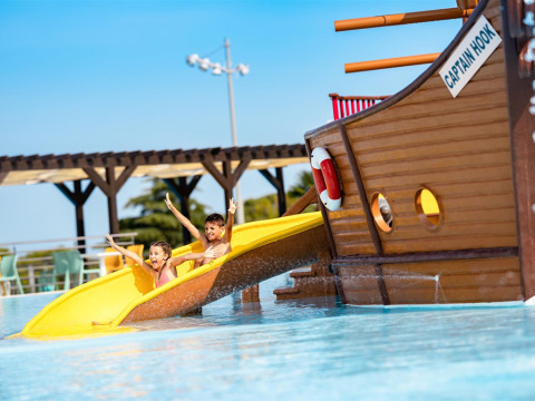 Two kids slide down a yellow waterslide by a pirate ship at Camping Park Umag holiday park in Istria, Croatia.