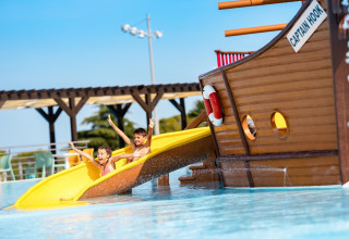 Two kids slide down a yellow waterslide by a pirate ship at Camping Park Umag holiday park in Istria, Croatia.