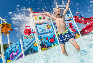 Ragazzo salta felice nell’acqua davanti all’area giochi colorata del Camping Park Umag, Istria, Croazia.