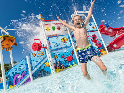 Ragazzo salta felice nell’acqua davanti all’area giochi colorata del Camping Park Umag, Istria, Croazia.