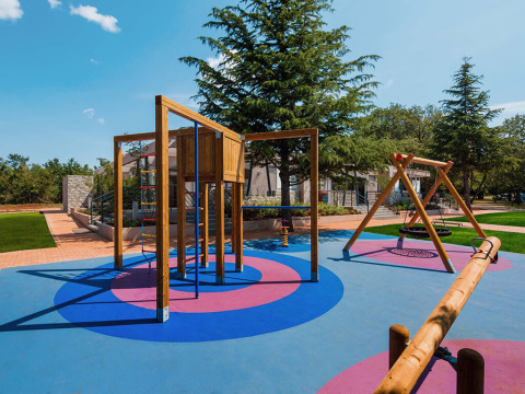 Playground with swings and climbing frame at Camping Park Umag in Istria, Croatia, surrounded by greenery.