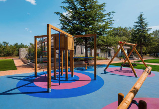 Parco giochi con altalene e struttura da arrampicata al Camping Park Umag in Istria, Croazia, tra il verde.