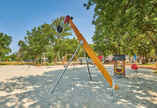 Legeplads med gynger og legeredskaber i Camping Park Umag, Istrien, Kroatien, omgivet af grønne træer.