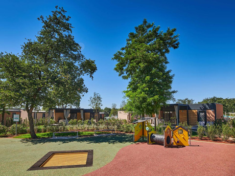 Area giochi con alberi e bungalow moderni presso Camping Park Umag, villaggio vacanze in Istria, Croazia.