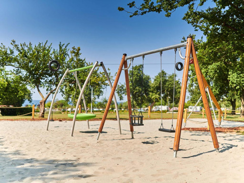Speeltuin met schommels en zand bij Camping Park Umag, een vakantiepark in Istrië, Kroatië, omgeven door bomen.