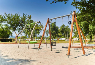 Spielplatz mit Schaukeln und Sand in Camping Park Umag, Ferienpark in Istrien, Kroatien, mit Bäumen.
