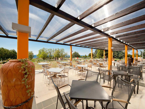 Area terrazza all’aperto al Camping Park Umag, Istria, Croazia, con tavoli, sedie e vista sul verde.