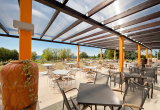 Area terrazza all’aperto al Camping Park Umag, Istria, Croazia, con tavoli, sedie e vista sul verde.
