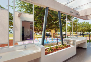 Modern outdoor washbasins with a view of a playground and green spaces at Camping Park Umag, Croatia.