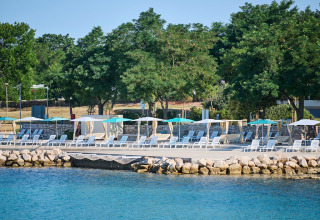 Tumbonas y sombrillas alineadas junto al agua en Camping Park Umag, Istria, Croacia, bajo un cielo azul.