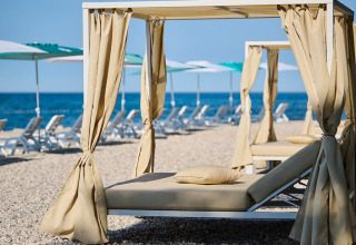 Luxus-Liegen mit Baldachin am Kiesstrand im Camping Park Umag, einer Ferienanlage in Istrien, Kroatien.