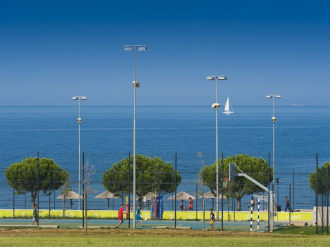 Children play basketball near the sea at Camping Park Umag, Istria, Croatia, with a sailboat in the background.