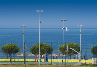 Children play basketball near the sea at Camping Park Umag, Istria, Croatia, with a sailboat in the background.