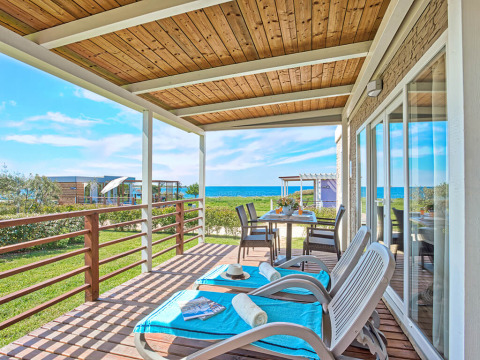 Sunny terrace at Park Riviera 2-bedroom lodge with sea view, loungers, outdoor dining and green lawn.