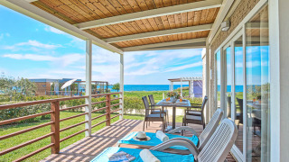 Sunny terrace at Park Riviera 2-bedroom lodge with sea view, loungers, outdoor dining and green lawn.