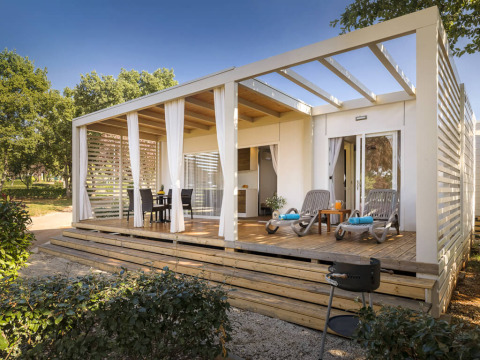 Lodge moderne Park Riviera EVO avec terrasse couverte, mobilier de jardin et transats dans un cadre vert.
